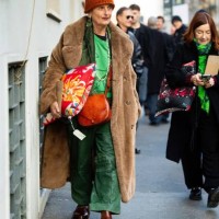 Guest wears a printed pillow as an accessor, an orange knitted hat, a beige teddy long coat, an orange leather crossbody bag, a green velvet blazer,...