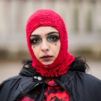 Guest wears a red embossed pattern hoodie, a black oversized nylon zipper bomber coat, a black and red print pattern long sleeves / legging jumpsuit,...