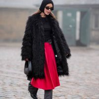 Guest wears a ribbed wool hood sunglasses, a black fluffy long coat, a black leather Coperni bag, a red skirt, gray striped flared pants, black...