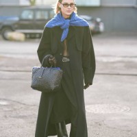 Guest wears a royal blue wool pullover worn as a scarf, a black long coat , a woven leather bag, outside The Garment, during the Copenhagen Fashion...