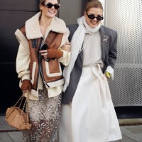 Guest wears a sheer long coat, white sweater, brown fur and leather vest, brown bag, and brown boots and a guest wears a white skirt, white sweater,...