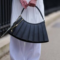 Guest wears a shiny black Lacoste leather bag, white outside Lacoste, during the Paris Fashion week Women's Fall/Winter 2025-2026 on March 9, 2025 in...