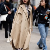 Guest wears a snake leather printed turtle neck shirt, a beige long trench and white leather heeled ankle boots outside Stella McCartney show during...