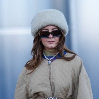 Guest wears a white fluffy chapka hat, sunglasses, a necklace, a green pullover , a beige padded oversized jacket, outside Munthe, during the...