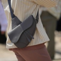 Guest wears a white latte denim with small striped print pattern jacket from Dior, a dark brown matte leather crossbody Saddle bag from Dior, brown...