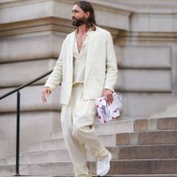 Guest wears a white latte V-neck shirt, a white latte blazer jacket, matching white latte suit large pants, a gold ring, white leather and fabric...