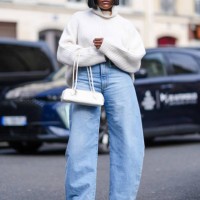 Guest wears a white oversized turtleneck ribbed wool pullover, sunglasses, blue denim wide-leg jeans / pants, white leather bag, black leather...