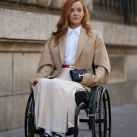 Guest wears a white shirt, a beige oversized blazer jacket, a belt, pleated skirt, a black mini Hermes bag, outside Hermes, during the Womenswear...