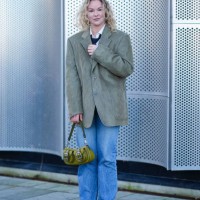 Guest wears a white shirt, black tie, a corduroy blazer jacket , a khaki green leather bag, blue denim jeans pants , brown pointed shoes, outside...