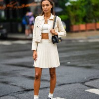 Guest wears a white shoulder-off / cropped top, a white latte buttoned jacket, a white latte embossed ribbed short skirt, a black shiny leather Boy...
