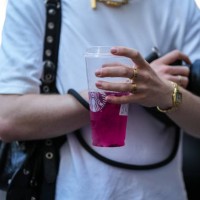 Guest wears a white t-shirt, a black shiny leather nailed / studded Cagole shoulder bag from Balenciaga, a gold watch, gold rings, gold Love rings...