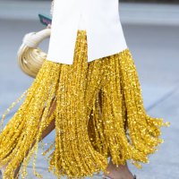 Guest wears a white top, a yellow long skirt made of paillettes fringes, silver and gold heeled sandals and a white and light yellow Bottega Veneta...