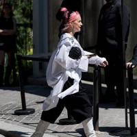 Guest wears an oversized white button-up shirt adorned with jeweled brooches and a silver chain detail, black wide-leg cropped trousers, white...