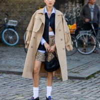 Guest wears animal print shorts, beige trench coat, blue button shirt, white socks, loafers outside Ganni during the Copenhagen Fashion Week...