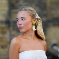 Guest wears beige black pattern head scarf, bright green and white earrings, white sheer mesh tube top, outside Deadwood, during the Copenhagen...