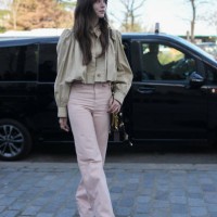 Guest wears beige cropped trench coat Chloe jacket, light pink high waisted loose Chloe denim jean pants, shiny black leather bag, gold rings,...