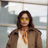 Guest wears beige top, neck scarf, yellow sunglasses and a brown leather jacket on day 1 of Visa Fashion Week Almaty 2024 on May 01, 2024 in Almaty,...