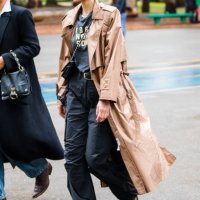Guest wears beige trench coat, graphic t-shirt, black cargo pants, tan boots, small black crossbody bag, hoop earrings, slicked-back hair at Sao...