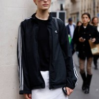 Guest wears black Adidas jacket, white mini skirt, outside The Row, during Womenswear Spring/Summer 2025 as part of Paris Fashion Week on September...