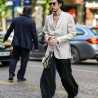 Guest wears black circle sunglasses, a white latte striped print pattern belted blazer jacket, rings, a beige and navy blue painted pattern leather...