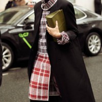 Guest wears black coat, checkered red white and blue dress and olive green bag outside the Loewe presentation during the Womenswear Fall/Winter...