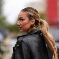 Guest wears black gold earrings, shiny black leather trench coat, outside Valentino, during the Paris Fashion week Spring/Summer 2025 on September...