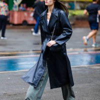 Guest wears black leather trench coat, white top, loose green wide-leg jeans, black sneakers, black crossbody bag with chain strap, minimalist style...