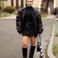 Guest wears black mini dress with a belt , leather jacket, long boots, black bag and a scarf wears during the 10th season of the Visa Fashion Week...