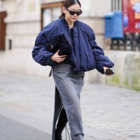 Guest wears black Saint Laurent / YSL sunglasses, a blue bomber jacket, black navy blue quilted velvet Chanel bag, a grey denim slit skirt, outside...