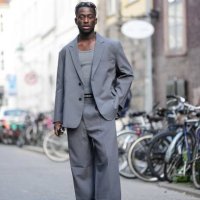 Guest wears black sport sunglasses, a gray tank-top, a gray oversized blazer jacket, matching gray large suit pants, white leather and gray suede...