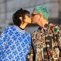 Guest wears black square sunglasses, silver earrings, a black high neck t-shirt, a blue and royal blue print pattern oversized pullover, a guest...
