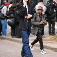 Guest wears black sunglasses, a black blazer jacket, a white top, a black leather bag, blue denim jeans / pants, black and white sneakers shoes,...