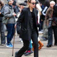 Guest wears black sunglasses, a black oversized blazer jacket, black pants, black gloves, black leather shoes, outside Dolce & Gabbana, during the...