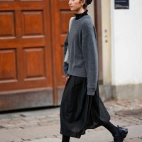 Guest wears black sunglasses, a black turtleneck top, a dark gray wool pullover, a pale gray leather shoulder bag, a black midi skirt, black tights,...