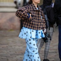 Guest wears black sunglasses, a dark brown and black checkered print pattern jacket, a pale blue with black and white circle print pattern ruffled...