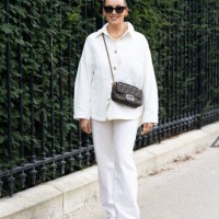 Guest wears black sunglasses, a Fendi cross-body Baguette bag, a gold necklace, white sneakers, a white jacket and white flared trousers outside...