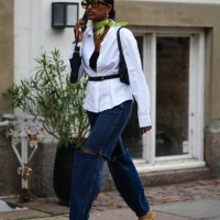 Guest wears black sunglasses, a green silk scarf, a white shirt, a black shoulder-off top, a black shiny leather shoulder bag, a black shiny leather...