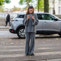 Guest wears black sunglasses, a grey wool turtleneck pullover, matchings pants, dark green sneakers shoes, during Womenswear Spring/Summer 2025 as...