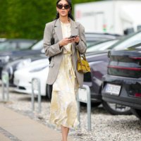 Guest wears black sunglasses, a pale gay long blazer jacket, a pale yellow with white embossed pattern long dress, a yellow shiny leather long...