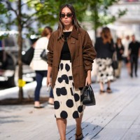 Guest wears black sunglasses, black shirt, white black polka dotted pattern/print pleated midi skirt, dark brown oversized jacket, shiny black...