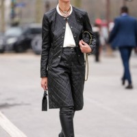 Guest wears black sunglasses, black silver Chanel choker necklace, white shirt, shiny black quilted Chanel leather jacket, gold bracelets, a gold...