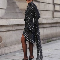 Guest wears black sunglasses, black white polka dotted sheer mesh high neck long sleeve mini dress, dark brown sheer mesh tights, shiny black pointed...