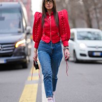 Guest wears black sunglasses, bright cherry red puffy sleeve zipped jacket, navy blue form fitting denim jean pants, gold bracelets, a black gold...