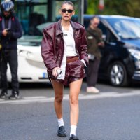 Guest wears black sunglasses, cream tank top, white unbuttoned long sleeve shirt, shiny dark red oversized biker leather jacket, dark brown leather...