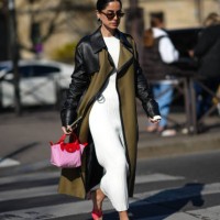 Guest wears black sunglasses, gold and rhinestones earrings, a white ribbed long dress, a khaki fabric and black leather shoulder long coat, a pink...