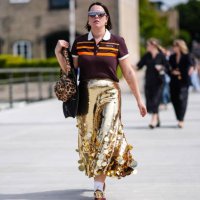 Guest wears black sunglasses, gold earrings, dark red brown bright orange striped Adidas Originals 80S short sleeve shirt, light brown and dark brown...