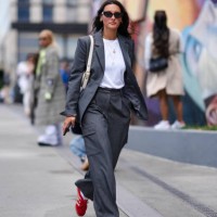 Guest wears black sunglasses, gold earrings, gold layered necklaces, white tank top, dark gray blazer jacket, cream bag, dark gray pants, bright red...
