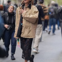 Guest wears black sunglasses, light brown / cream jacket, a black lace skirt with floral details, black sneakers shoes, outside Hermes, during...