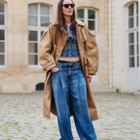 Guest wears black sunglasses, navy blue buttoned up denim jean jacket, light brown trench coat, navy blue washed loose denim jean pants, outside...