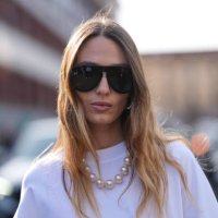 Guest wears black sunglasses, pearl necklace, white oversized black print Moschino shirt, outside Moschino, during the Milan Fashion week Women's...